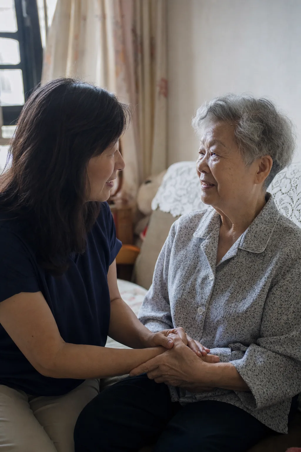 An adult daughter gently holding her elderly mother's hands at home